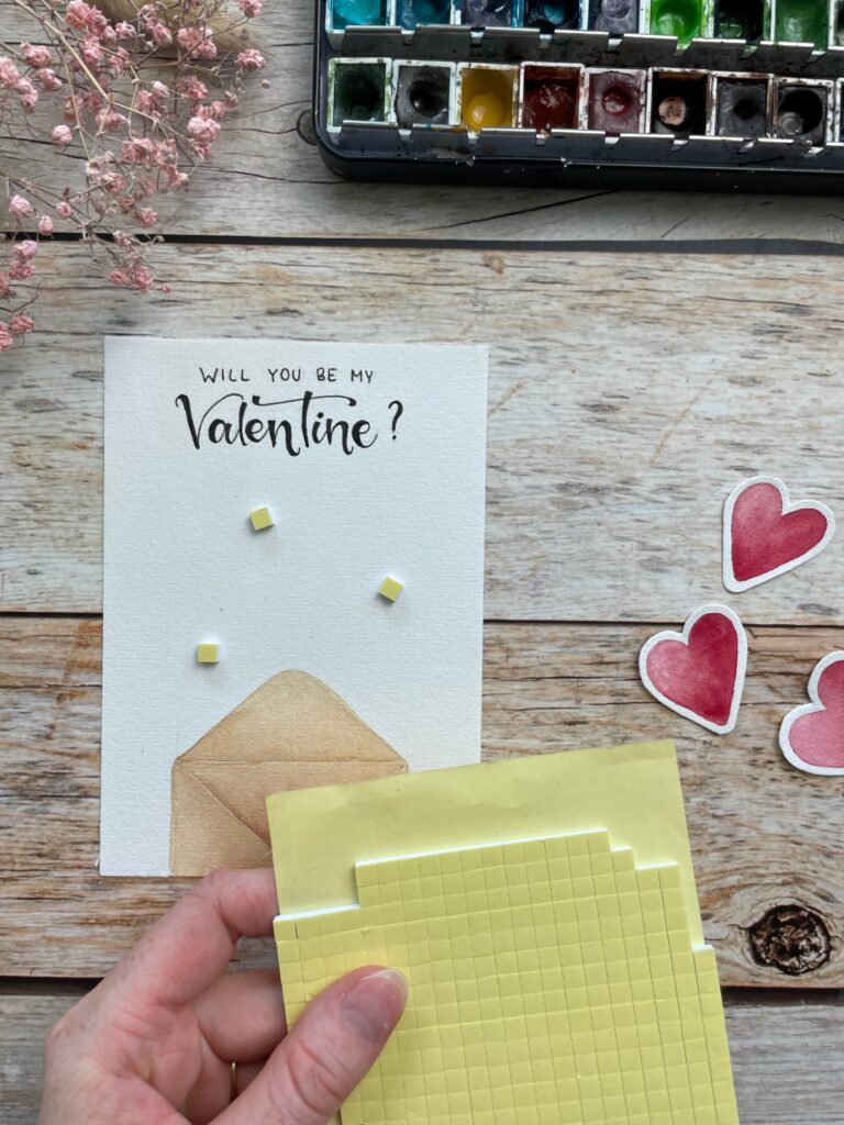 Eine Karte zum Valentinstag mit einem Briefumschlag und dem Spruch "Will you be my Valentine" Es wird gezeigt, wie man Abstandsklebepads anbringt.