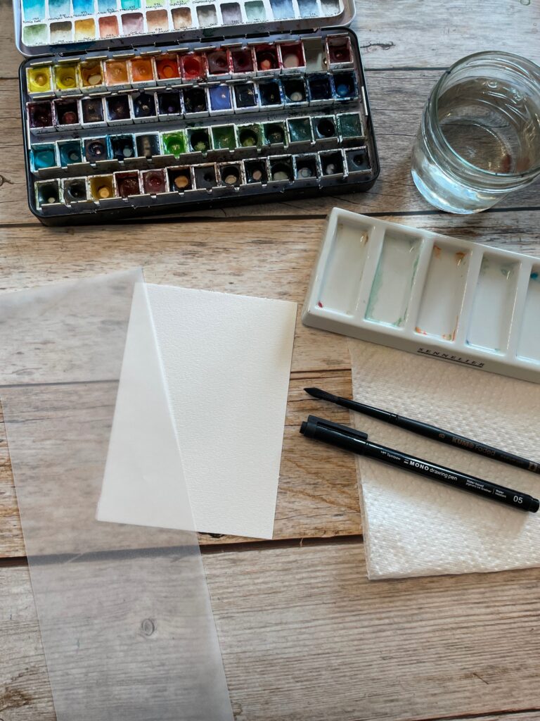 Auf dem Bild sind die Materialien für die Osterkarte ersichtlich. Aquarellpapier im DIN A6 Format, Fineliner, Aquarellpinsel, Aquarellfarben, Mischpalette, Wasser und Transparentpapier