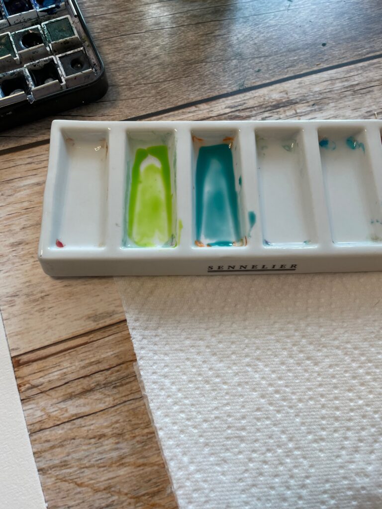 Auf dem Bild ist die Mischpalette mit zwei frühlingshaften Aquarellfarben, helles grün und türkis, zu sehen.