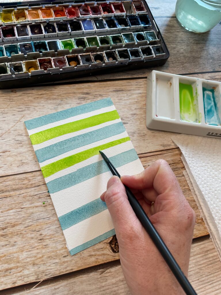 Die Zwischenräume der türkisen Aquarellstreifen werden nun mit grünen Streifen gefüllt